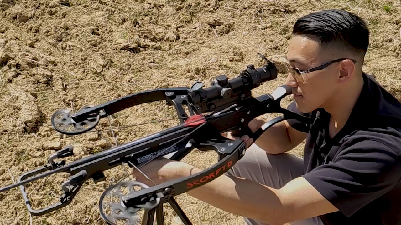 Chris crouches with cocked crossbow and scope